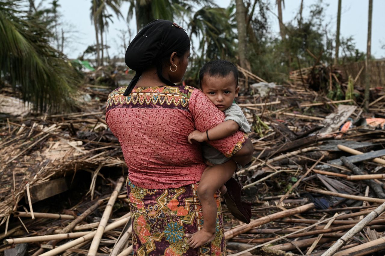 A Rohingya woman carries her baby next to her destroyed home at the Basara refugee camp in Sittwe, Myanmar, on Tuesday, May 16.