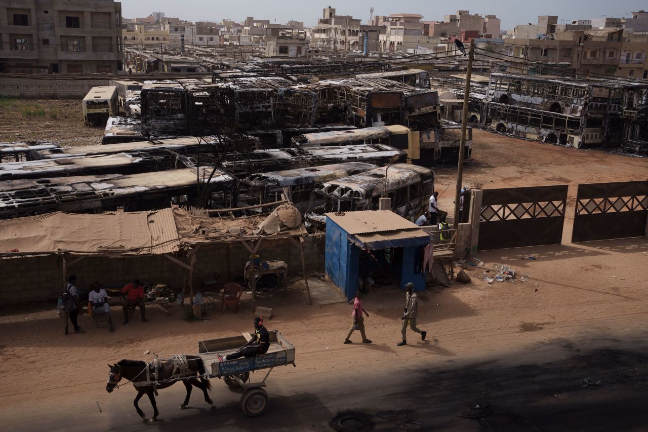 A man drives a horse-drawn cart past burned buses in Keur Massar, Senegal, on Wednesday, May 16. The service vehicles were set on fire by protesters the night before, when supporters of Senegalese opposition leader Ousmane Sonko clashed with security forces.