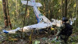 In this photo released by Colombia's Armed Forces Press Office, a soldier stands in front of the wreckage of a Cessna C206, Thursday, May 18, 2023, that crashed in the jungle of Solano in the Caqueta state of Colombia.  A search continues for four Indigenous children who may have survived the deadly plane crash in the Amazon jungle on May 1. On Tuesday, May 16, soldiers found the wreckage and the bodies of three adults, including the pilot and the children's mother. 