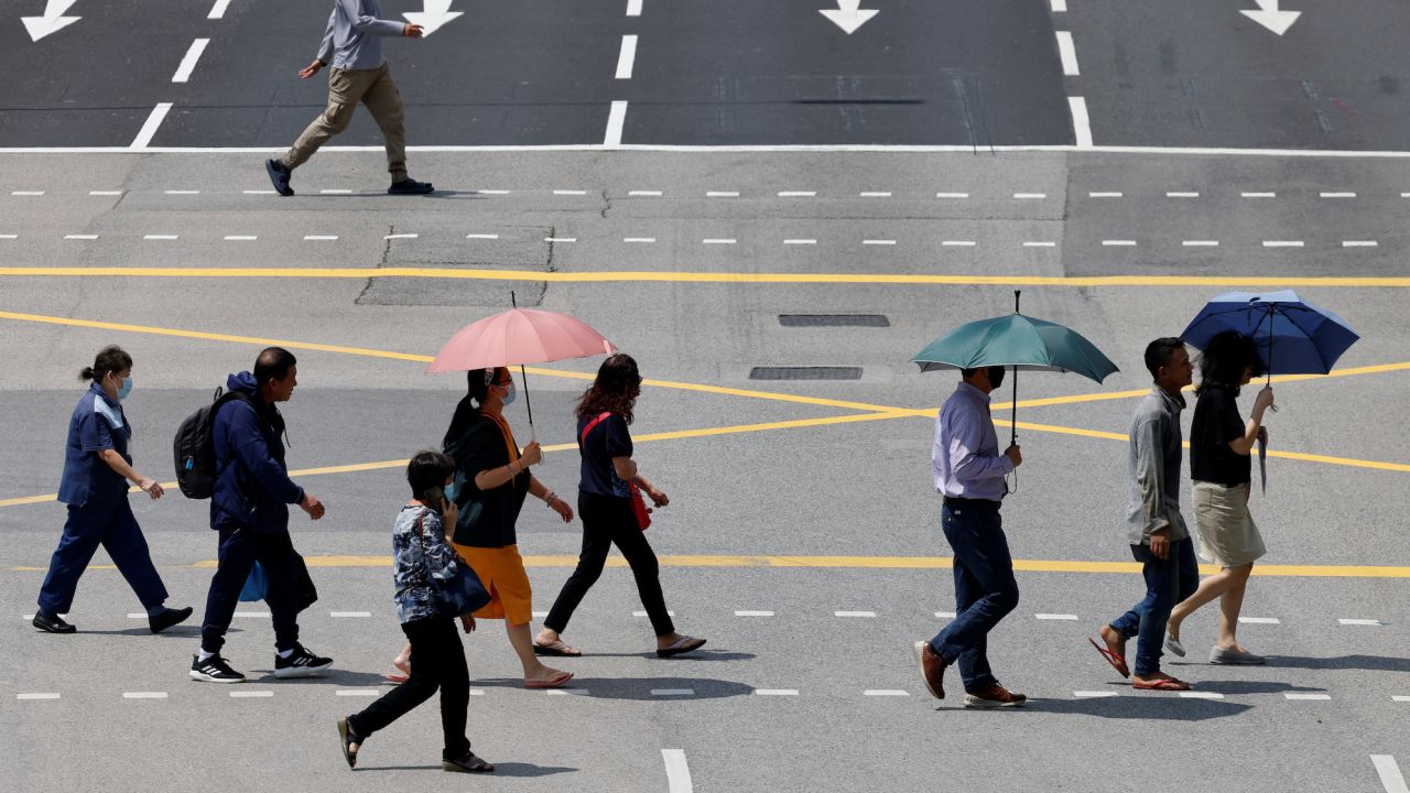 People in Singapore shield themselves with umbrellas from the glaring sun as they cross a street.