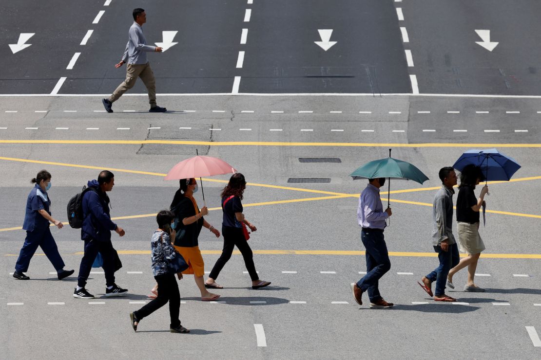 People in Singapore shield themselves with umbrellas from the glaring sun as they cross a street.