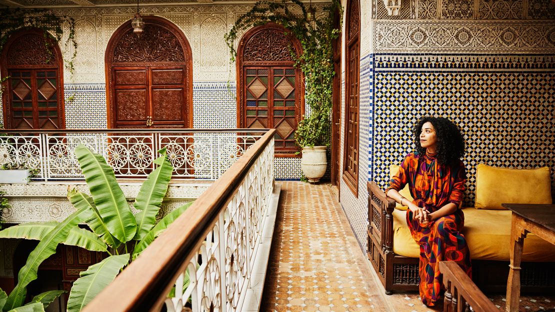 Wide shot of smiling woman relaxing in alcove of ornately decorated riad while on vacation in Marrakech