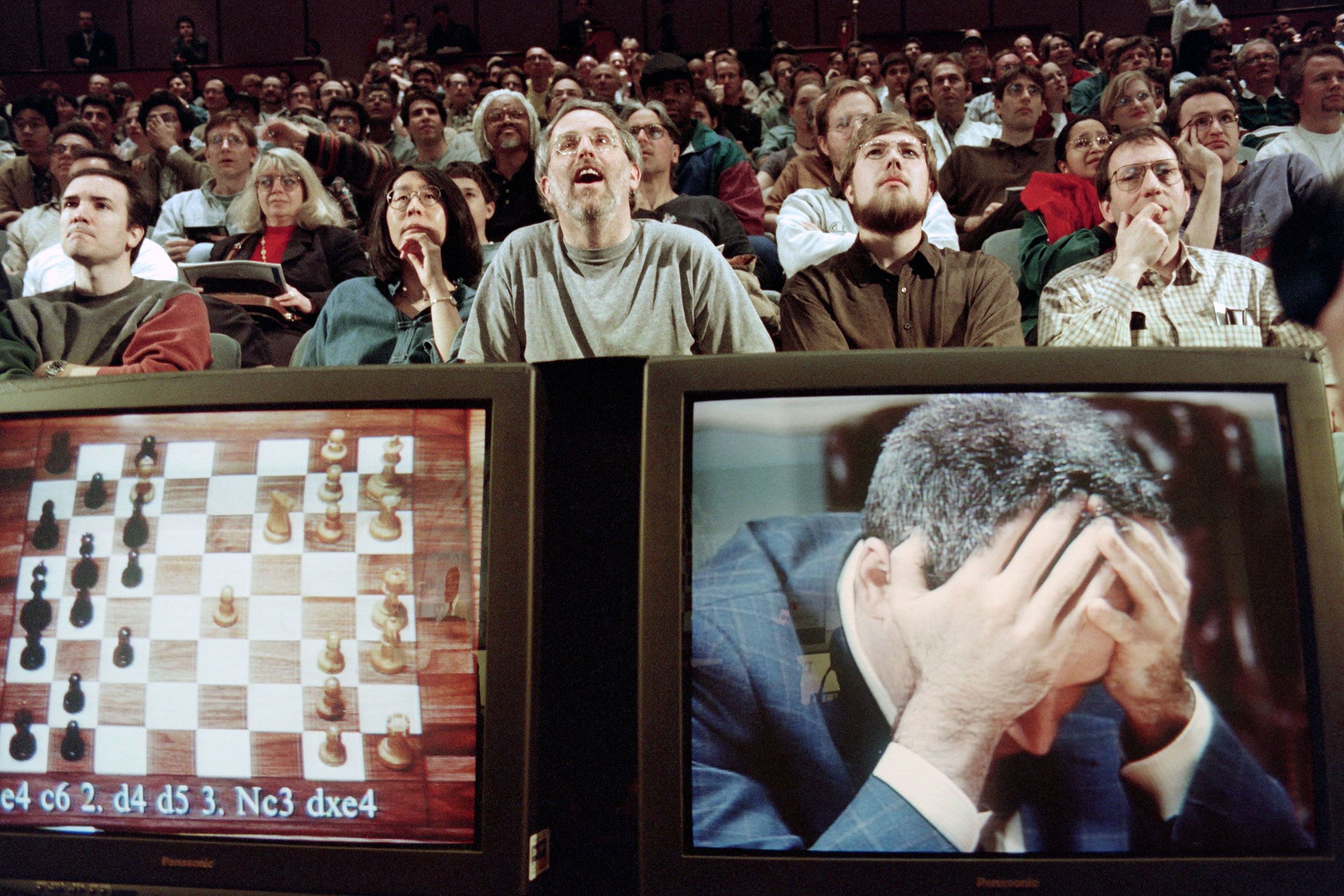 Chess enthusiasts watch World Chess champion Garry Kasparov on a television monitor as he holds his head in his hands at the start of the sixth and final match  May 11, 1997 against IBM's Deep Blue computer in New York. Kasparov lost this match in just 19 moves giving overall victory to Deep Blue with a score of 2.5-3.5.
