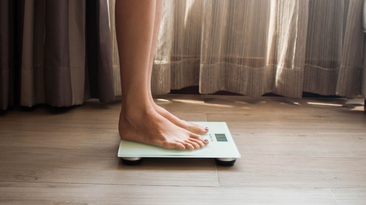 A low-angle view of a young woman who is weighing herself in a weighing scale