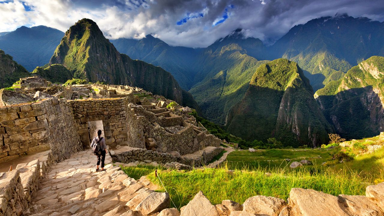 Back view of female tourist descending stairs overlooking Machu Picchu ruins at sunset, Peru