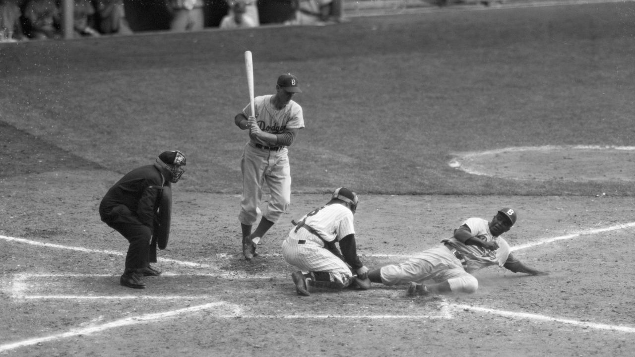 Auf einem Aktenfoto vom 28. September 1955 ist Jackie Robinson (rechts) sicher unter einem versuchten Out des Yankee-Fängers Yogi Berra, der von der dritten Base nach Hause stiehlt.  Pinch-Hitter Frank Kellert (L) wartet darauf, zu schlagen.  Die Yankees besiegten die Dodgers mit 6:5.