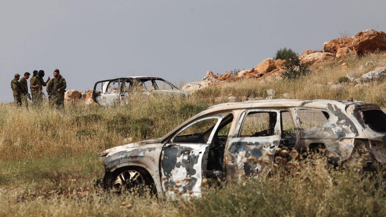 Israeli soldiers stand next to a car, reportedly burnt by Israeli settlers, in the village of Al-Mughayer, east of the occupied West Bank city of Ramallah on May 26, 2023. 