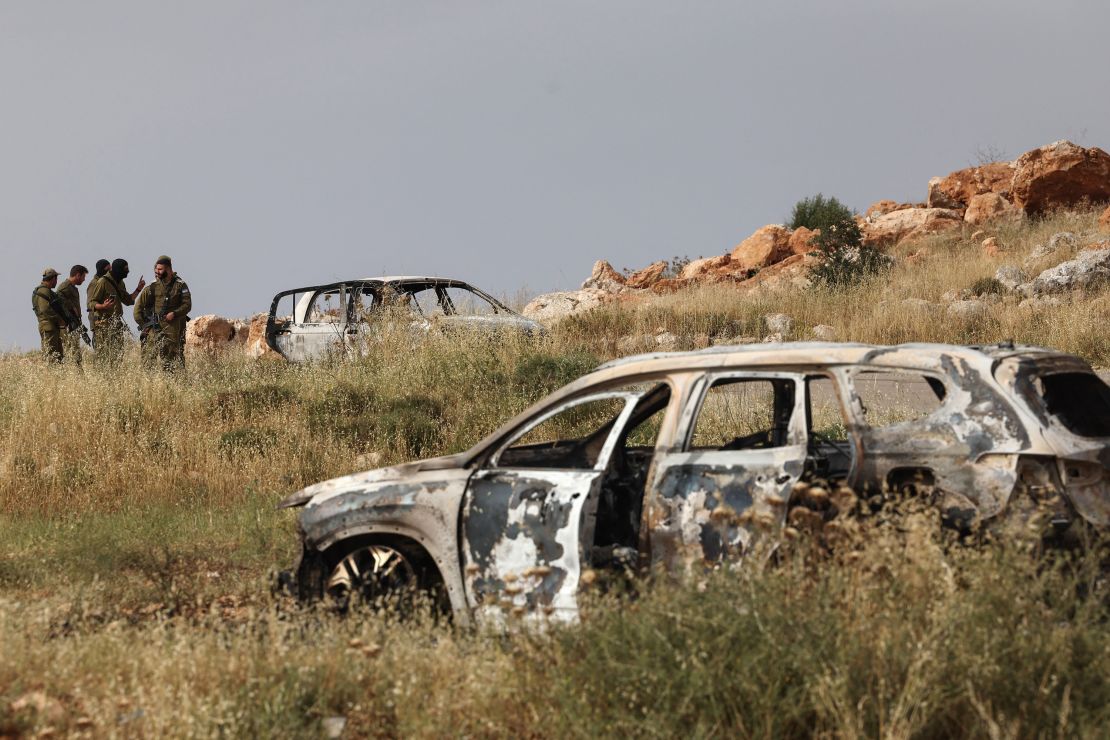 Israeli soldiers stand next to a car, reportedly burnt by Israeli settlers, in the village of Al-Mughayer, east of the occupied West Bank city of Ramallah on May 26, 2023. 