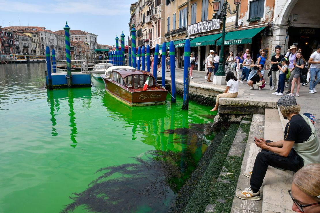 People observe Venice's historical Grand Canal as a patch of phosphorescent green liquid spreads in it,.