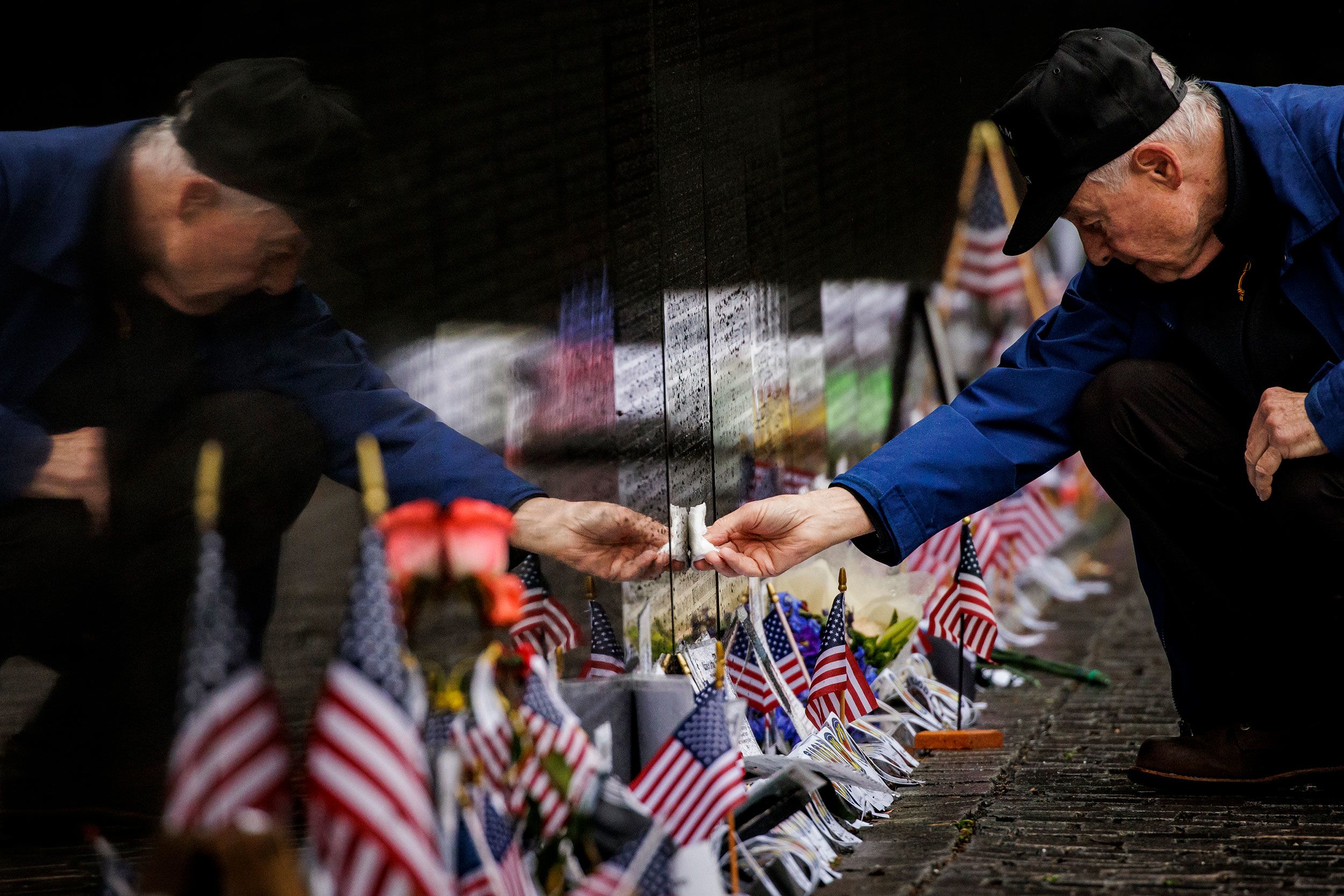 David Loesch, a Vietnam War veteran, wipes rainwater from a soldier's name on the Vietnam Veterans Memorial in Washington, DC.