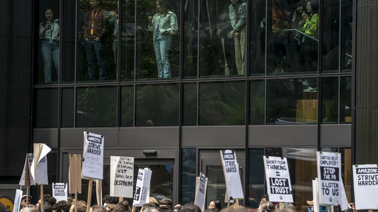 People watch from inside Amazon's Day One building as Amazon workers hold signs during a walkout event at the company's headquarters on May 31, 2023 in Seattle, Washington. The protest action was organized to call attention to return to office requirements, in addition to recent layoffs and climate change issues. 