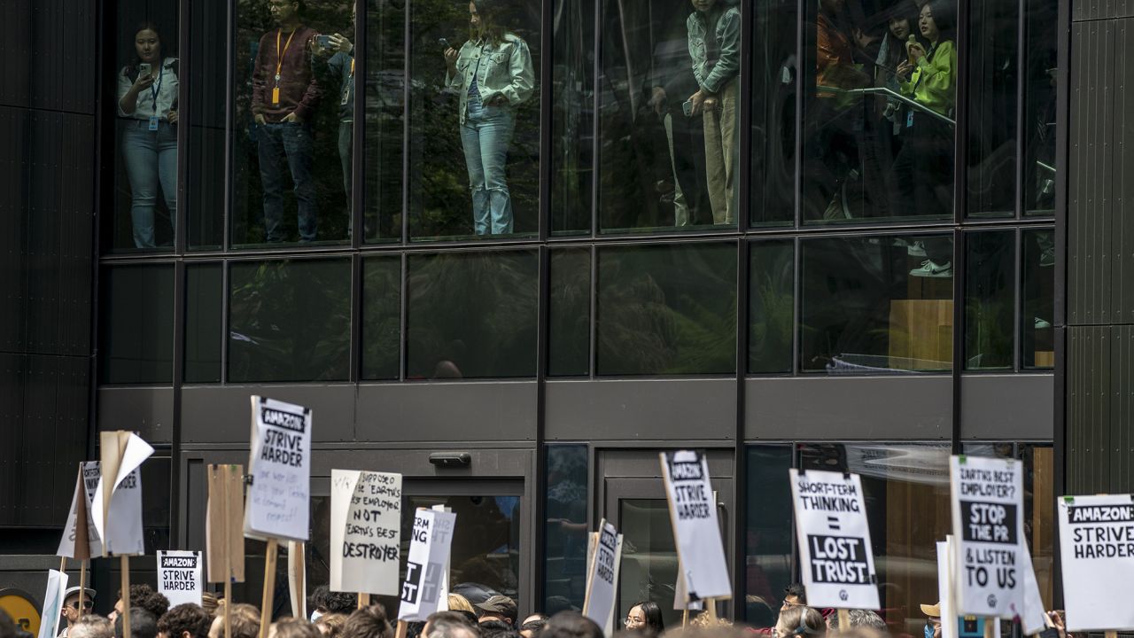 People watch from inside Amazon's Day One building as Amazon workers hold signs during a walkout event at the company's headquarters on May 31, 2023 in Seattle, Washington. The protest action was organized to call attention to return to office requirements, in addition to recent layoffs and climate change issues.