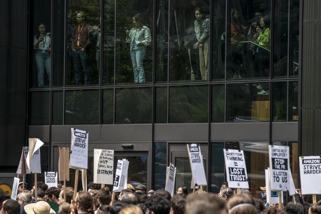 People watch from inside Amazon's Day One building as Amazon workers hold signs during a walkout event at the company's headquarters on May 31, 2023 in Seattle, Washington. The protest action was organized to call attention to return to office requirements, in addition to recent layoffs and climate change issues. 