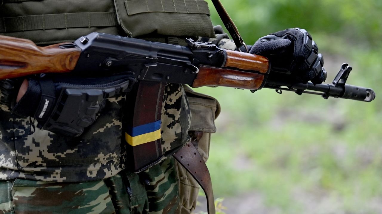A fighters of the territorial defence unit, a support force to the regular Ukrainian army, holds a Kalshnikov gun decorared with Ukrainian flag ribbon during an exercise as part of the regular combat tactics classes, not far from the Ukrainian town of Bucha, Kyiv region on June 17, 2022. (Photo by Sergei SUPINSKY / AFP) (Photo by SERGEI SUPINSKY/AFP via Getty Images)