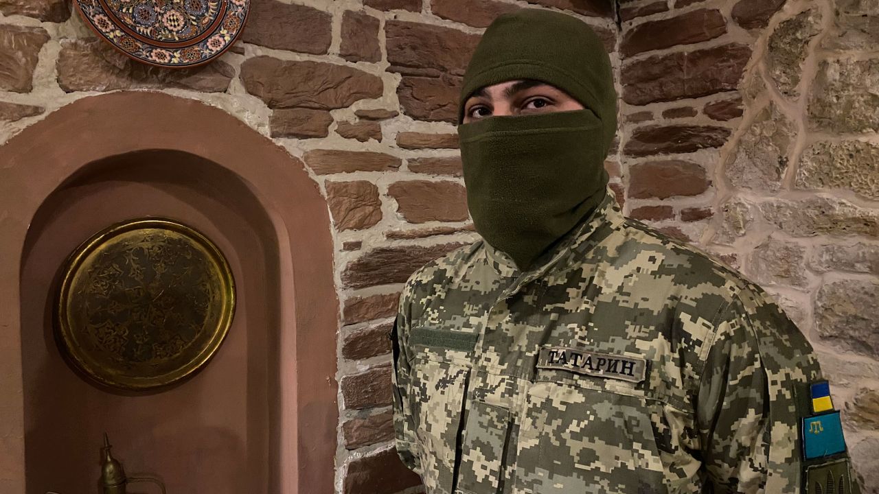 Viktor Shevchenko, in combat uniform, shows patches on his arm bearing the flags of Ukraine and the Crimean Tatars.
