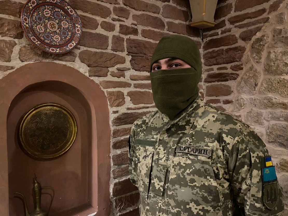 Viktor Shevchenko, in combat uniform, shows patches on his arm bearing the flags of Ukraine and the Crimean Tatars.