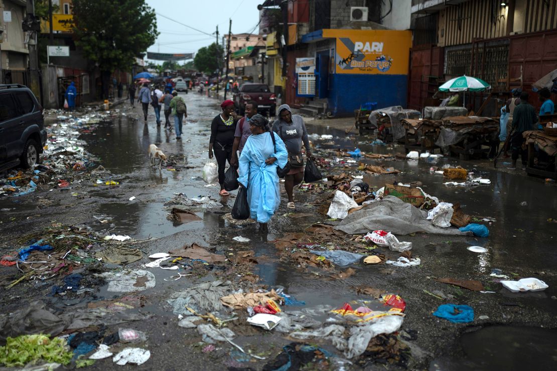 People make their way through puddles while walking in the middle of a street littered with garbage following heavy rains in Port-au-Prince.