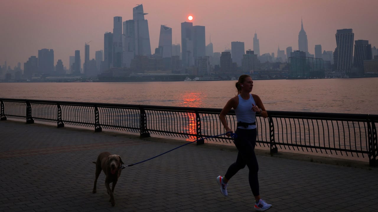 A woman jogs with a dog along the Hudson River shortly after sunrise, as haze and smoke caused by wildfires in Canada hang over the Manhattan skyline, in New York City, New York, U.S., June 7, 2023. REUTERS/Mike Segar