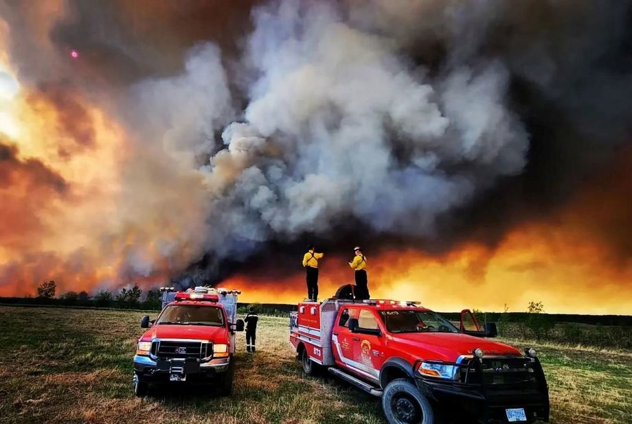 Firefighters stand on a truck while battling a blaze near Fort St. John, British Columbia, on May 14.