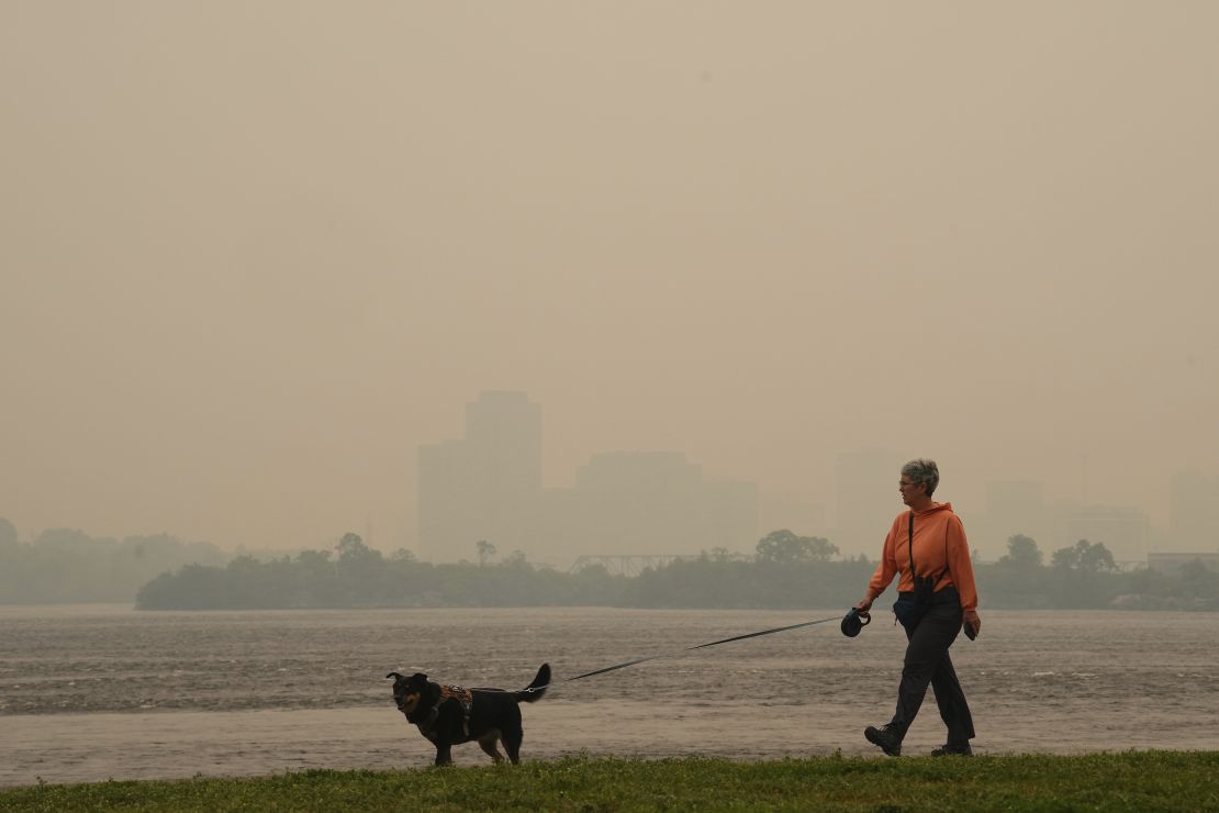 A woman walks her dog Tuesday along the Ottawa River in Ottawa as smoke obscures Gatineau, Quebec.