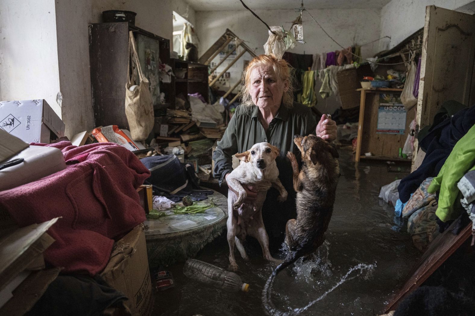 Local resident Tetiana holds her pets, Tsatsa and Chunya, as she stands inside her flooded house after the destruction of the dam.