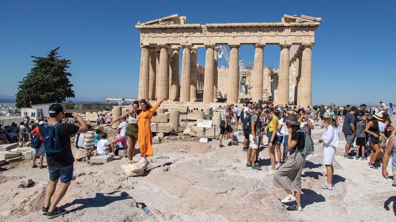Tourists are posing for a picture with the Parthenon. Crowds of tourists and local visitors in front of the Parthenon, an ancient temple dedicated to the goddess Athena, on the Akropolis of Athens on the known sacred rock. People are seen walking and takings pictures of the ancient monument, while wearing hats because of the Greek sun. The Acropolis of Athens is an ancient citadel located on a rocky outcrop above the city of Athens and contains the remains of several ancient buildings of great architectural and historical significance, the most famous being the Parthenon attracting millions of tourists and visitors every year. It was built in 432BC by the architects Iktinos and Calicrates with famous sculptures from Phidias inside. Acropolis is a UNESCO World Heritage Site. Greece is facing an increased wave of tourist arrivals in pre pandemic levels, as of summer 2022 the numbers are exceeding the era before the COVID-19 Coronavirus travel restriction measures. Tourism is one of the main income sources of the country. Athens, Greece on July 2022 (Photo by Nicolas Economou/NurPhoto via Getty Images)