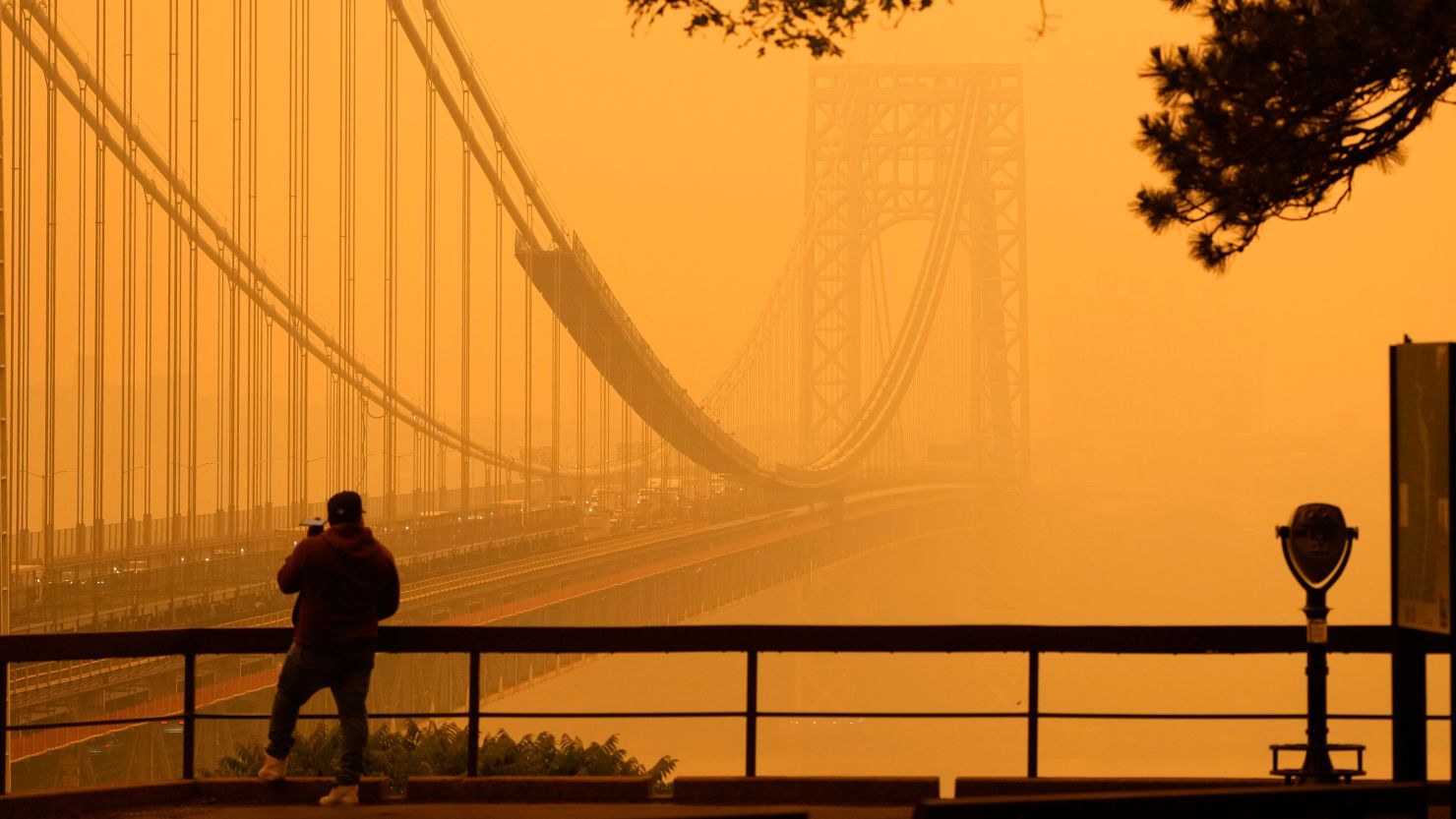 A person talks on his phone as he looks through the haze at the George Washington Bridge from Fort Lee, New Jersey, Wednesday, June 7, 2023.