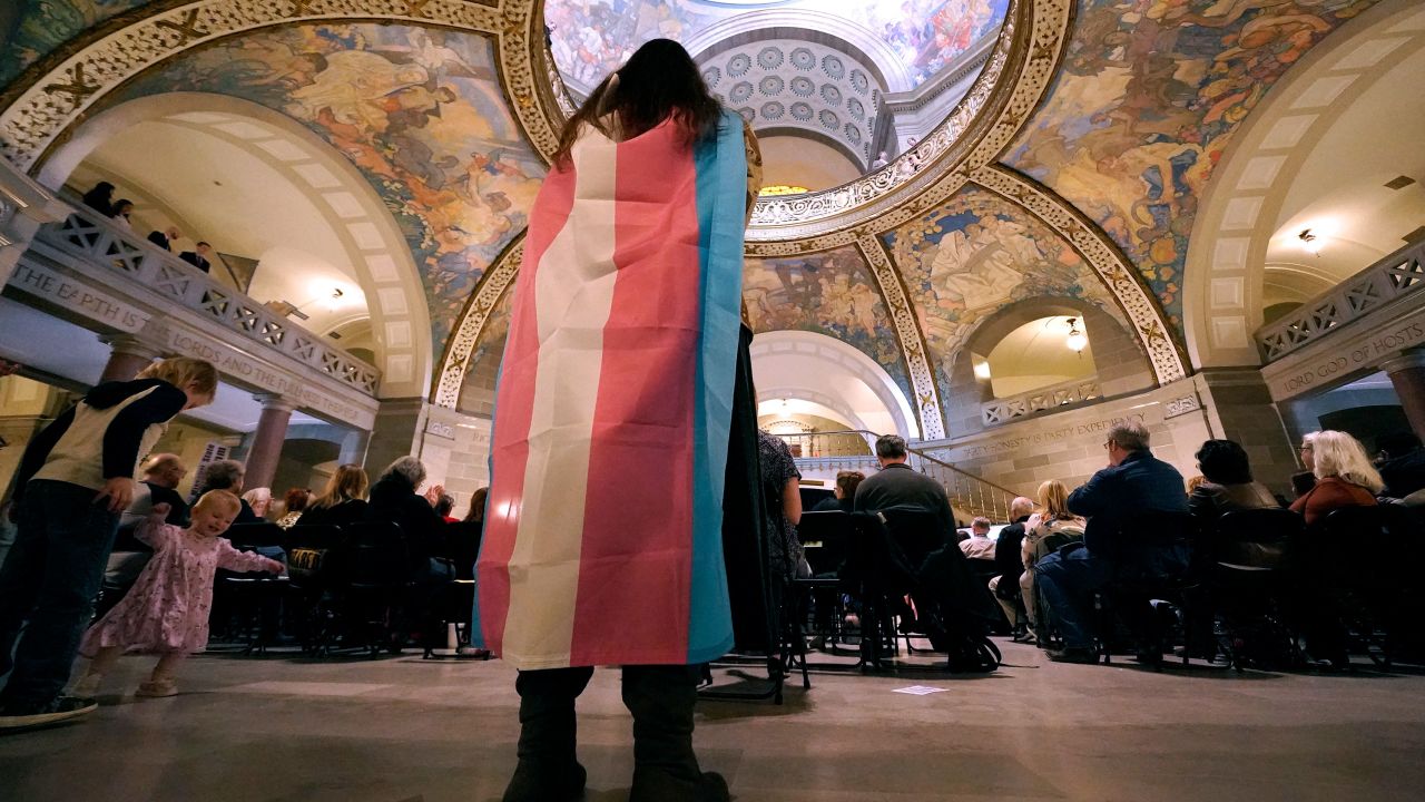 FILE - Glenda Starke wears a transgender flag as a counter protest during a rally in favor of a ban on gender-affirming health care legislation, March 20, 2023, at the Missouri Statehouse in Jefferson City, Mo. Transgender minors and some adults in Missouri will soon be banned from accessing puberty blockers, hormones and gender-affirming surgeries under a bill signed Wednesday, June 7, 2003, by the state's Republican governor. (AP Photo/Charlie Riedel, File)