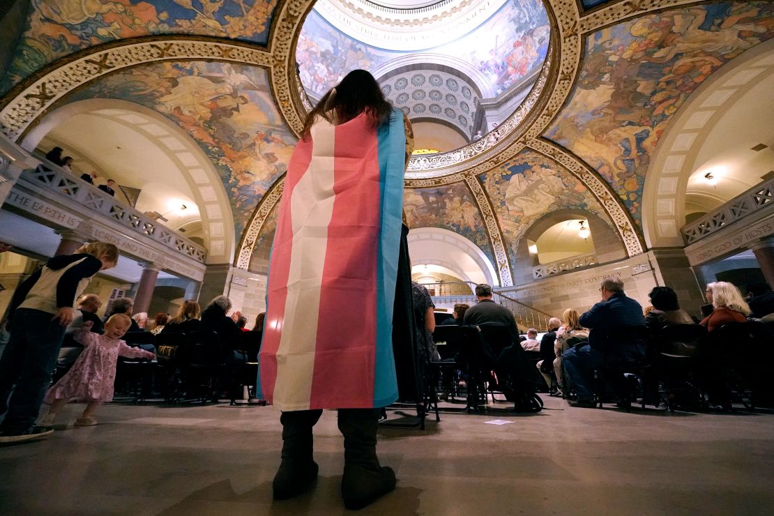 FILE - Glenda Starke wears a transgender flag as a counter protest during a rally in favor of a ban on gender-affirming health care legislation, March 20, 2023, at the Missouri Statehouse in Jefferson City, Mo. Transgender minors and some adults in Missouri will soon be banned from accessing puberty blockers, hormones and gender-affirming surgeries under a bill signed Wednesday, June 7, 2003, by the state's Republican governor. (AP Photo/Charlie Riedel, File)