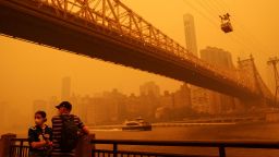People wear protective masks as the Roosevelt Island Tram crosses the East River while haze and smoke from the Canadian wildfires shroud the Manhattan skyline in the Queens Borough New York City, on June 7.