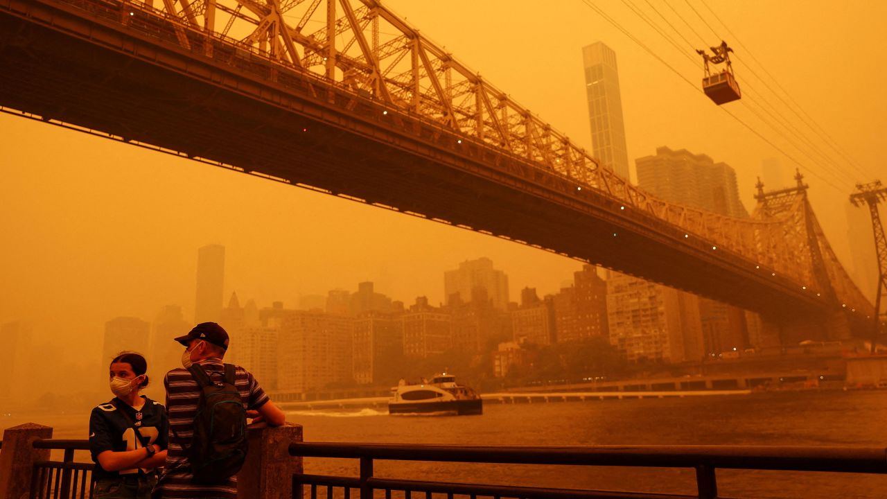 People wear protective masks as the Roosevelt Island Tram crosses the East River while haze and smoke from the Canadian wildfires shroud the Manhattan skyline in New York City on June 7.