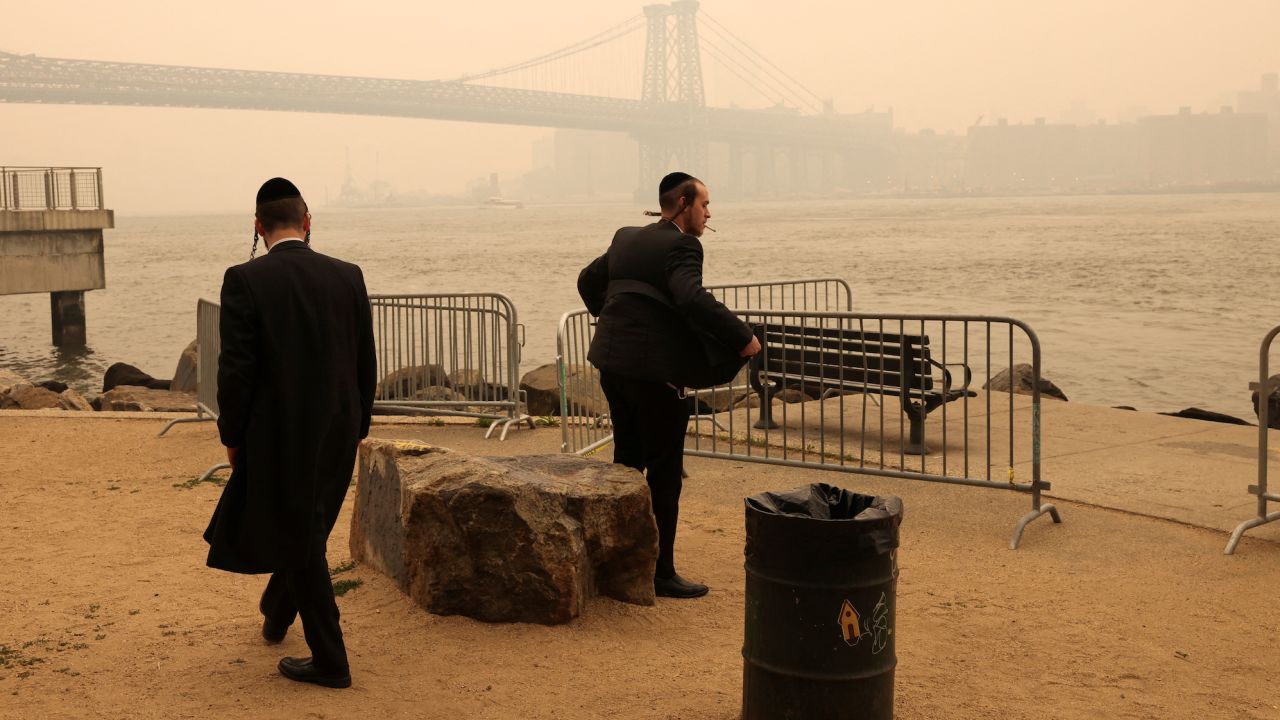 Two Orthodox Jewish men stand with by the waterfront as haze and smoke caused by wildfires in Canada cover the Manhattan Skyline, in Brooklyn, New York, on Wednesday.