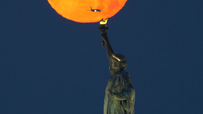 NEW YORK, NY - JUNE 04: The full Strawberry Moon sets behind the Statue of Liberty before sunrise on June 4, 2023, in New York City. (Photo by Gary Hershorn/Getty Images)