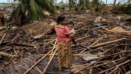 A Rohingya woman carries her baby next to her destroyed house at Basara refugee camp in Sittwe on May 16, 2023, after cyclone Mocha made a landfall. 