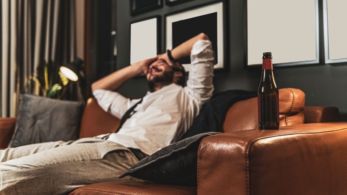 Side view of young man sitting in sofa at his living room , he enjoys beer after long working day from home