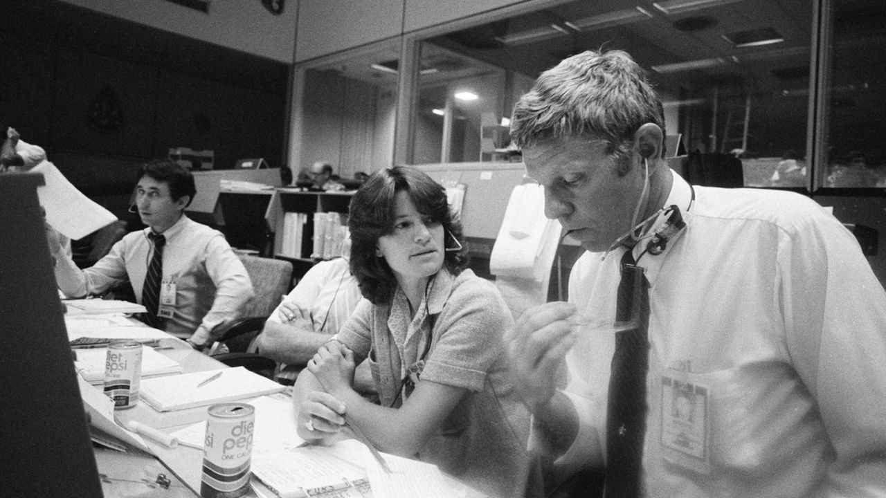 S81-33963 (July 1981) --- Mission Specialist/Astronaut Sally K. Ride and Dale E. Moore of the Flight Control Division's Electrical, Mechanical and Environmental Systems Division are particularly interested in a simulation session during which the Remote Manipulator System (RMS, a mechanized Arm) takes the spotlight for a moment.  You are seated at the CAPCOM or capsule comms console in the mission control room of the JSC's Mission Control Center.  dr  Ride will chat with astronauts Joe H. Engle and Richard H. Truly during their STS-2 mission in space when the RMS will make its debut in the Columbia's cargo hold.  Astronaut James F. Buchli, serving in a CAPCOM capacity, is partially behind Dr.  Ride hidden.