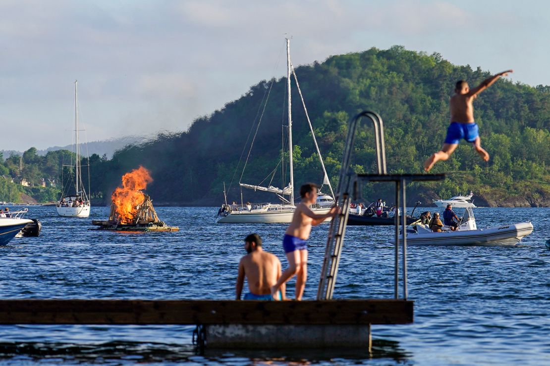 A floating bonfire burns marking midsummer celebrations as people jump in to the water from a diving platform in the Oslo Fjord by Bjorvika on June 23, 2022. - Norway OUT (Photo by Håkon Mosvold Larsen / NTB / AFP) / Norway OUT (Photo by HAKON MOSVOLD LARSEN/NTB/AFP via Getty Images)