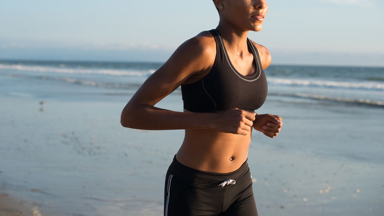 Black woman runs along the beach by the ocean