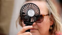 A Houston Astros fan uses a hand fan to keep cool while waiting to enter Minute Maid Park in Houston, Texas, for a baseball game against the Cincinnati Reds on Saturday, June 17, 2023.