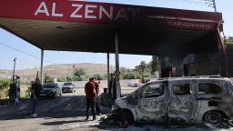People stand near a burnt car, reportedly set ablaze by Israeli settlers, at a gas station in Al-Lubban Al-Gharbi in the occupied West Bank on June 21, 2023. Four people were shot and killed yesterday near a settlement in the occupied West Bank, Israeli officials said, a day after an army raid in the territory left six Palestinians dead. (Photo by AHMAD GHARABLI / AFP) (Photo by AHMAD GHARABLI/AFP via Getty Images)