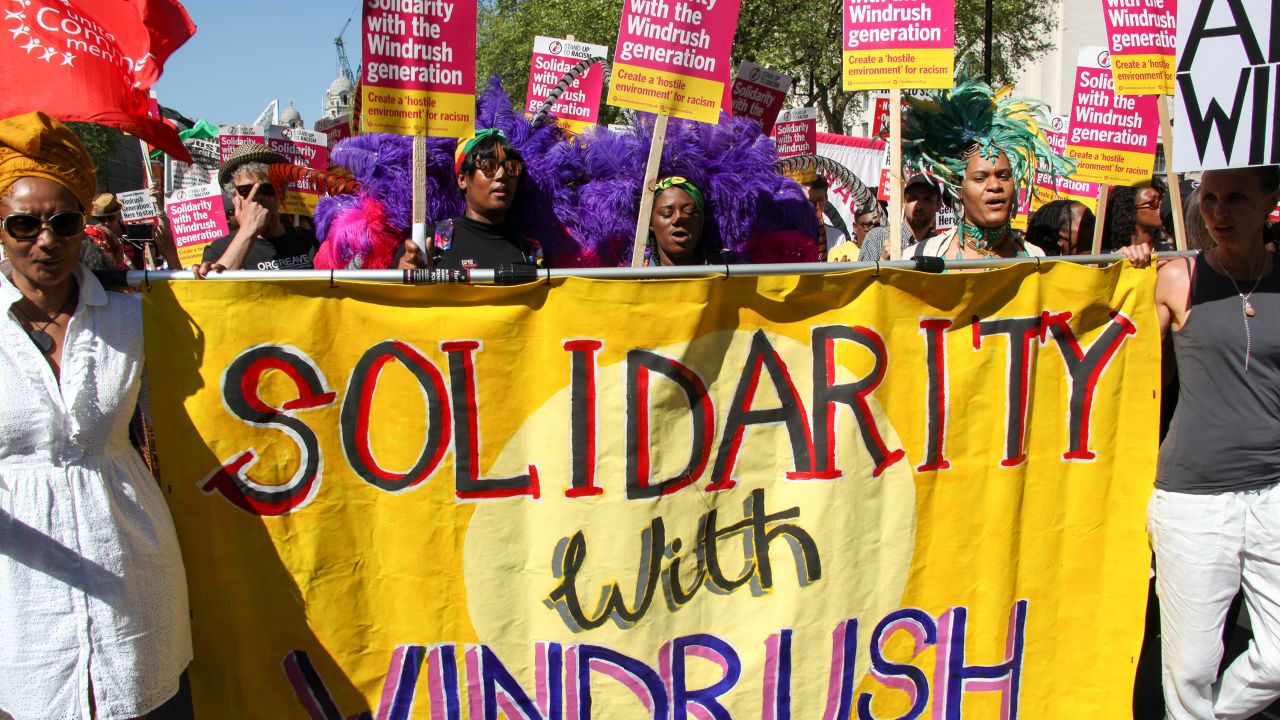 Protesters hold a sign reading "Solidarity with Windrush."