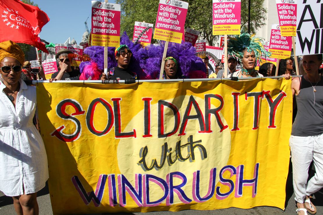Protesters hold a sign reading "Solidarity with Windrush."