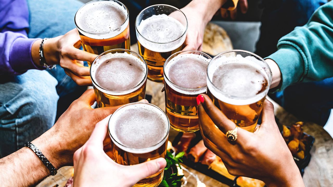 Multiracial group of young people cheering glass of beer together at brewery pub- Happy friends enjoying summer drinking blonde pint sitting at bar table- Food and beverage concept-Youth culture