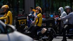 A delivery rider drinks water as she and other motorists wait to cross a street on a hot day in Beijing, Wednesday, June 21, 2023. 