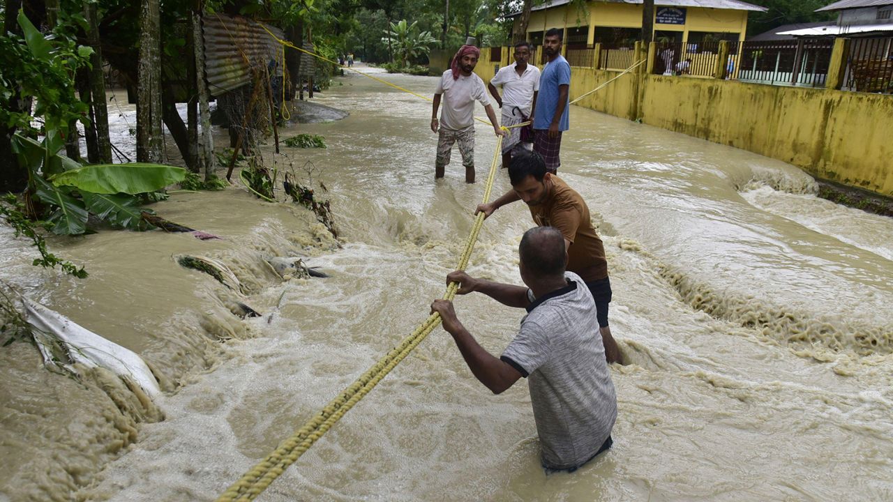 Men trying to cross the flooded street in Nalbari district of Assam India on Tuesday June 21, 2023.
