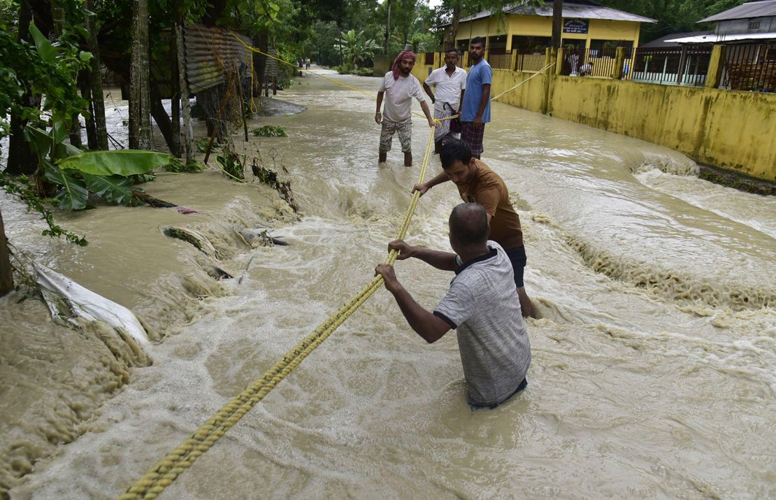 Men trying to cross the flooded street in Nalbari district of Assam India on Tuesday June 21, 2023.