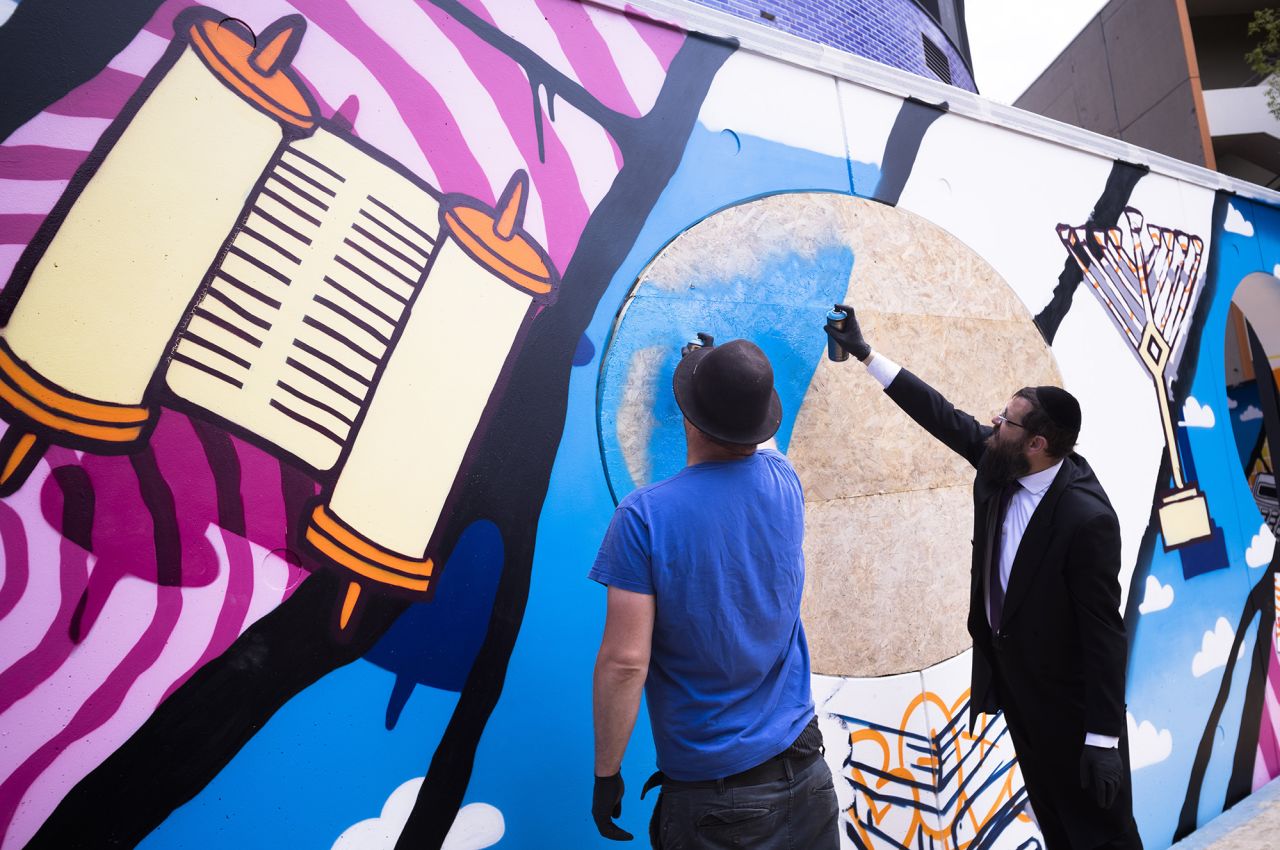 Rabbi Yehuda Teichtal, right, and artist Tobo, left, spray paint on a graffiti wall on the campus.