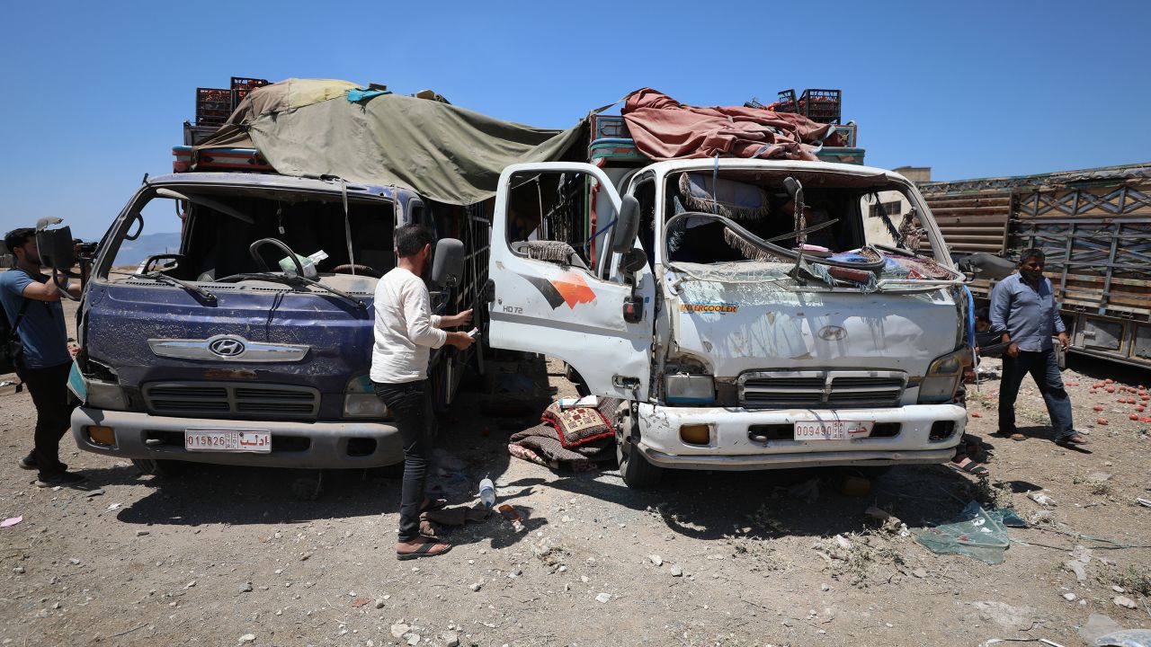People stand next to damaged trucks at the market in Idlib following the Russian airstrike.