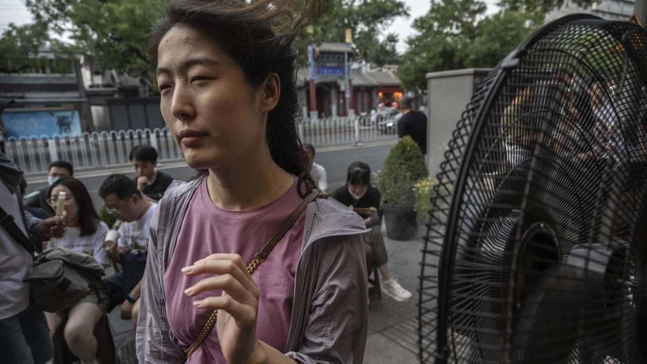 A woman cools herself on a misting fan as she waits for a table outside a popular local restaurant during a heatwave on June 23, 2023 in Beijing, China.