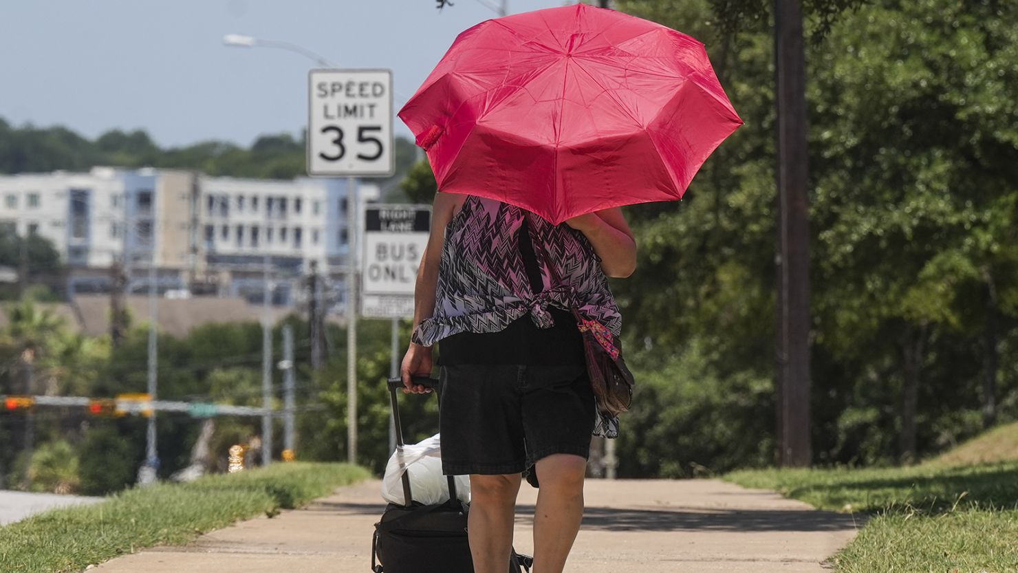 A woman walks with an umbrella to shield herself from the sun along East Riverside Drive in Austin on Monday. 